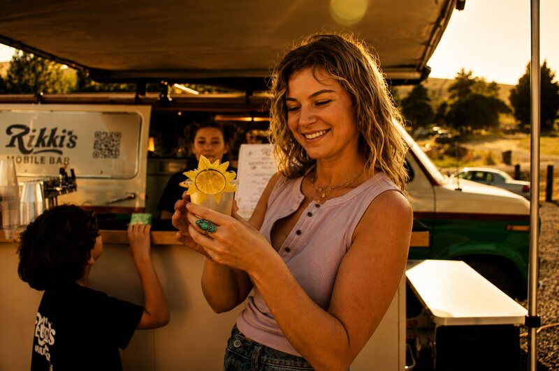 Guest smiling with a sunflower-garnished cocktail in front of Rikki's mobile bar